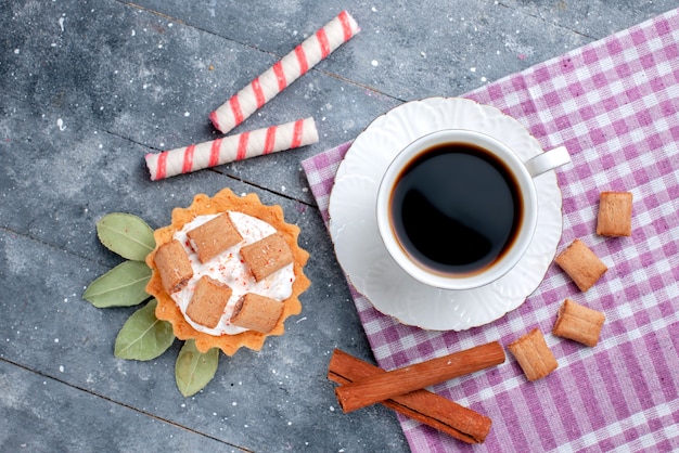 Vista superior de la taza de café caliente y fuerte junto con pastel y canela en gris, bebida dulce de caramelo de café