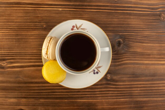 Vista superior de una taza de café caliente y fuerte con macarons franceses en el escritorio rústico de madera marrón café bebida caliente