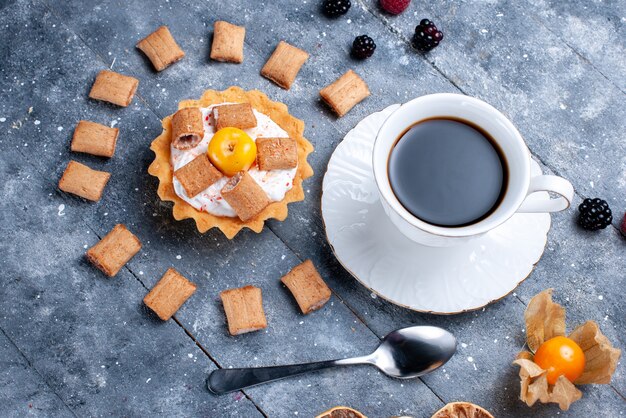 Vista superior de una taza de café con una cremosa almohada de pastel formada galletas junto con bayas en gris, color de la foto de galleta de baya