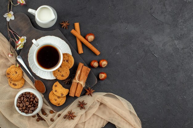 Vista superior taza de café cuchara de galletas de anís sobre tablero de madera granos de café en un tazón sobre una superficie oscura
