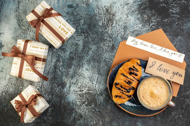 Vista superior de una taza de café y deliciosas cajas de regalo hermosas croisasant frescas para su amado en una superficie oscura