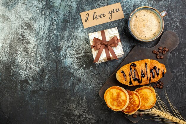 Vista superior de una taza de café y un delicioso desayuno fresco hermosa caja de regalo panqueques croisasant sobre fondo oscuro