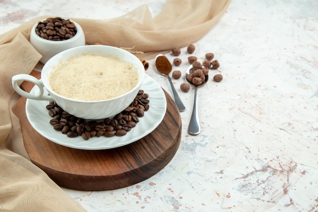 Vista superior de una taza de café y frijoles, limas de canela molidas, toalla de color nude en el lado derecho sobre fondo blanco