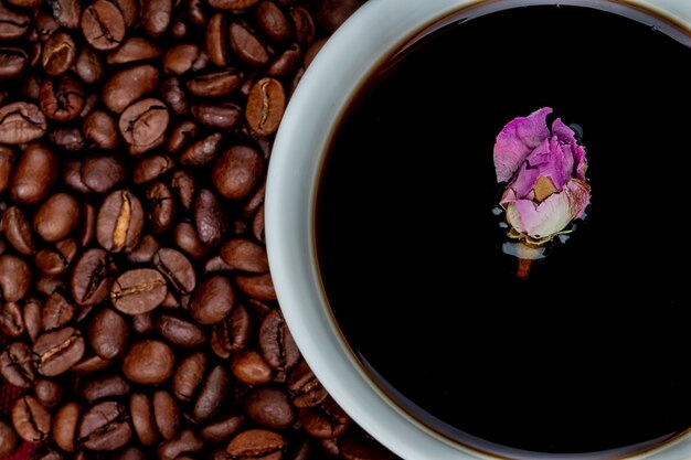 Foto gratuita vista superior de una taza de café con granos de café y capullo de rosa de té