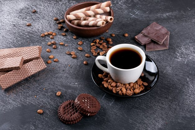 Vista superior de la taza de café con granos de café y diferentes galletas en la mesa oscura