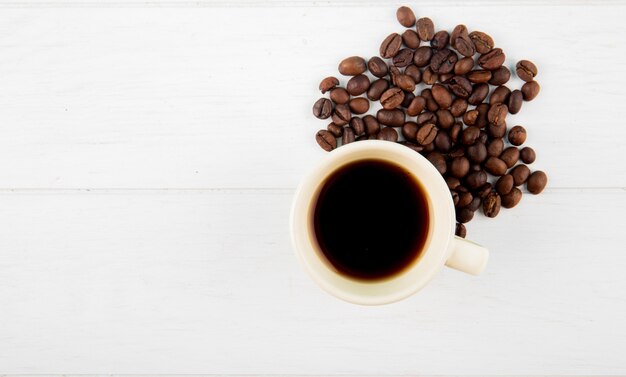 Vista superior de una taza de café y granos de café esparcidos sobre fondo blanco con espacio de copia