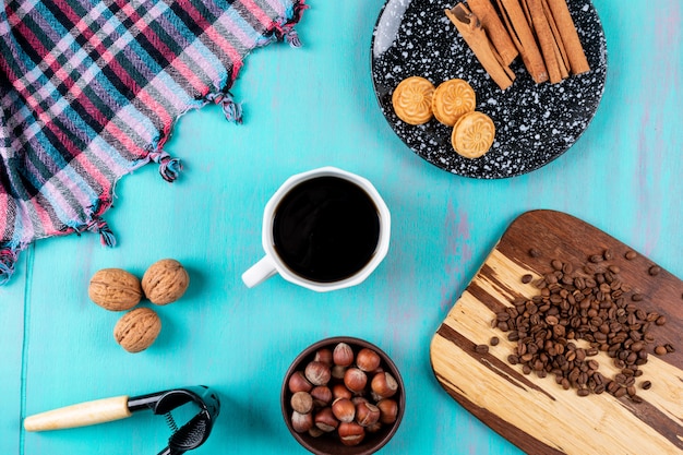 Vista superior taza de café con granos de café galletas y nueces en mesa azul