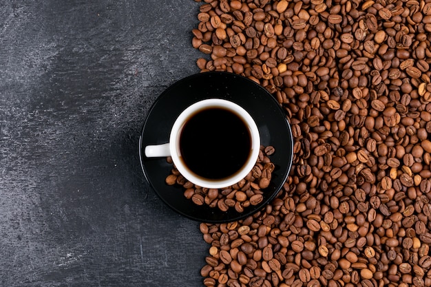 Vista superior de la taza de café y granos de café en la mesa oscura