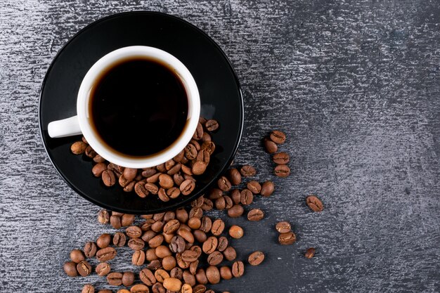 Vista superior de la taza de café con granos de café en la mesa oscura