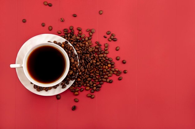 Vista superior de una taza de café con granos de café tostados frescos aislado sobre un fondo rojo con espacio de copia