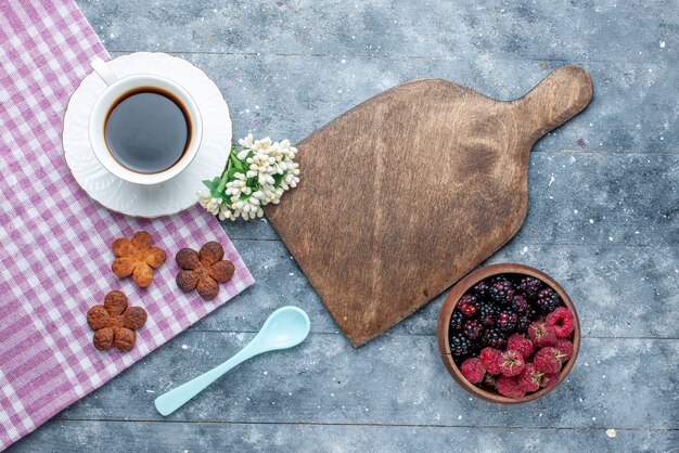 Vista superior de la taza de café junto con las bayas de las galletas en madera gris, galleta de la galleta de los pasteles del azúcar dulce hornear