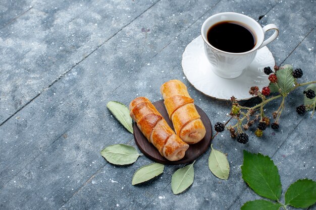 Vista superior de la taza de café junto con deliciosos brazaletes en madera gris, azúcar de pastel de pastelería dulce hornear