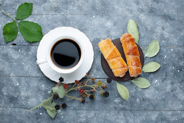 Vista superior de la taza de café junto con dulces y deliciosos brazaletes bayas en madera gris, dulce hornear pastel de azúcar