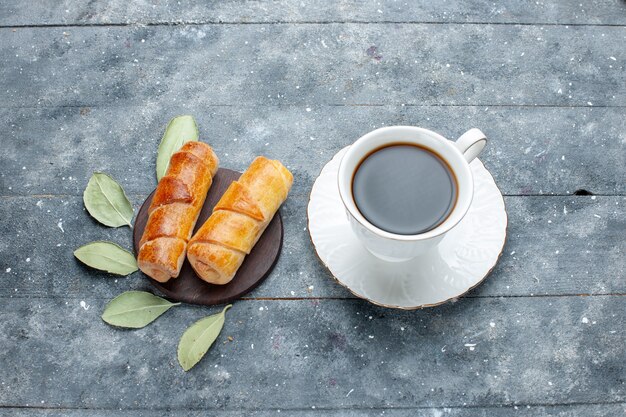 Vista superior de la taza de café junto con dulces deliciosos brazaletes en madera gris, pastel de pastelería dulce hornear