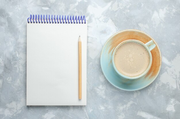 Vista superior de la taza de café con leche dentro de la taza con el bloc de notas en el escritorio blanco beber café leche color del escritorio