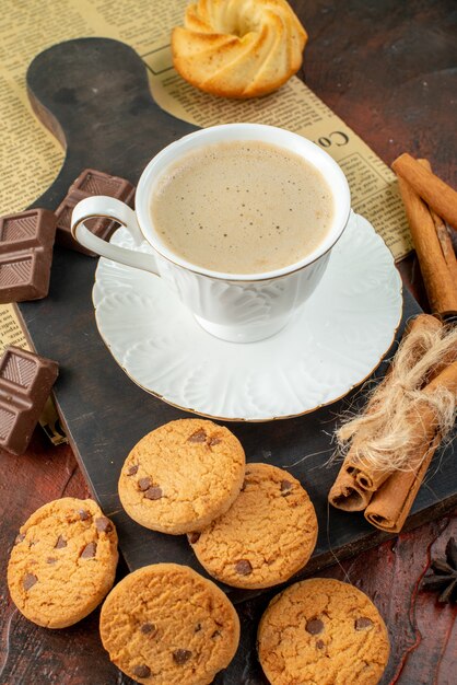 Vista superior de la taza de café en la tabla de cortar de madera en un periódico antiguo galletas canela limas barras de chocolate sobre fondo oscuro