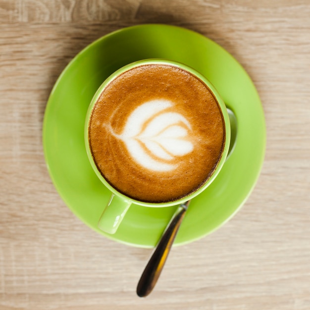 Vista superior de la taza de café verde con arte hermoso del latte sobre superficie de madera