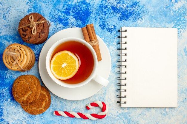 Vista superior de una taza de galletas de té atadas con un bloc de notas de cuerda en la mesa azul