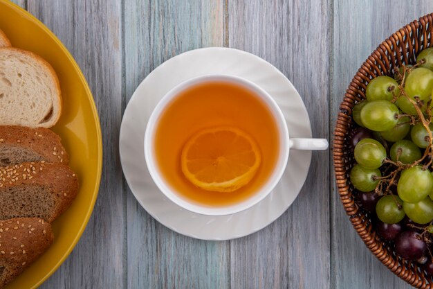 Vista superior de la taza de hot toddy con rebanadas de pan en plato y canasta de uva sobre fondo de madera