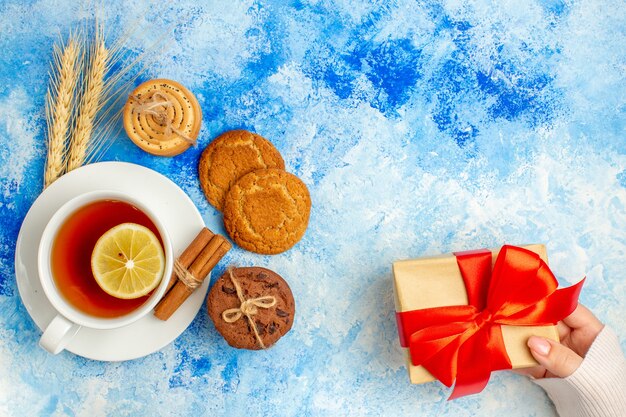 Vista superior taza de regalo de galletas de té en mano femenina en lugar libre de mesa azul