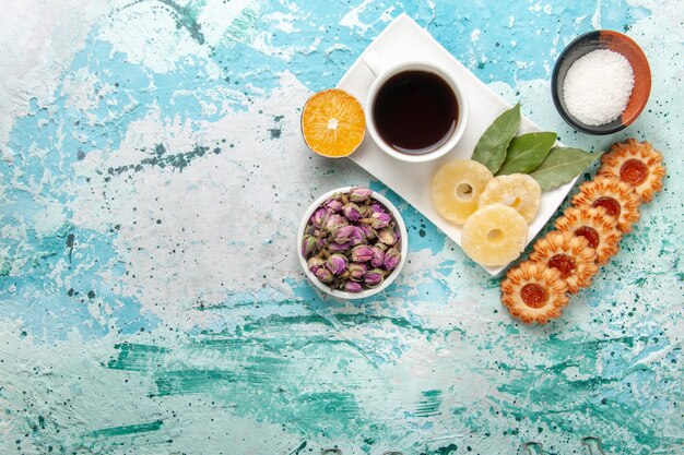 Vista superior de una taza de té con anillos de piña secos y galletas en la superficie azul claro