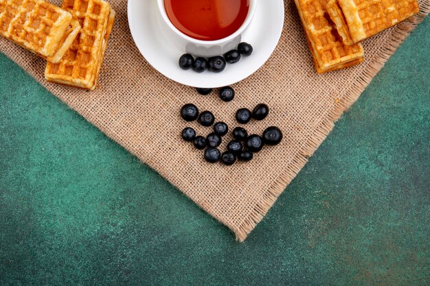 Vista superior taza de té con arándanos y gofres sobre un fondo verde