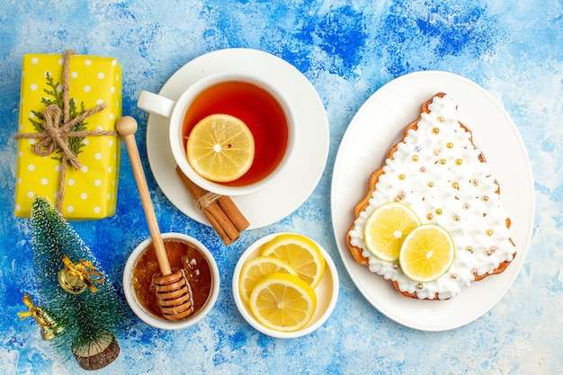 Vista superior taza de té árbol de Navidad pastel en placa rodajas de limón miel en mesa azul