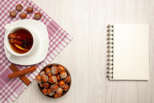 Vista superior de una taza de té con avellanas y canela en el color blanco de la merienda de té de nuez de escritorio