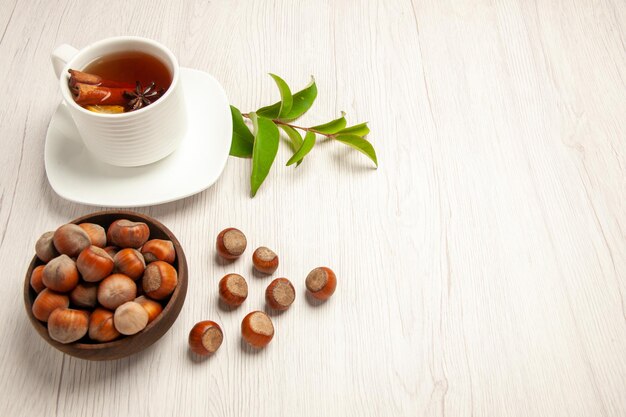 Vista superior de la taza de té con avellanas frescas en la ceremonia de aperitivos de frutos secos de té de escritorio blanco