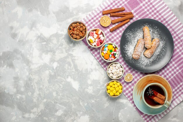 Vista superior de la taza de té con bagels y caramelos sobre superficie blanca