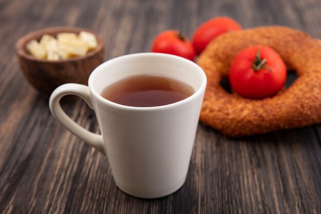 Vista superior de una taza de té con bagels turcos y tomates rojos frescos aislados sobre un fondo de madera