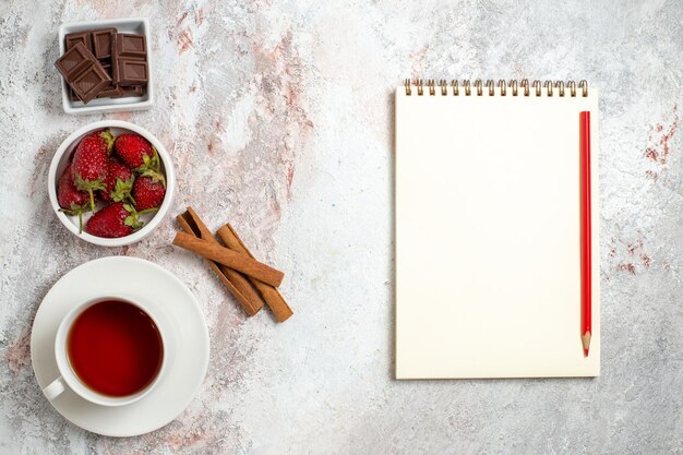 Vista superior de la taza de té con bayas de canela sobre superficie blanca