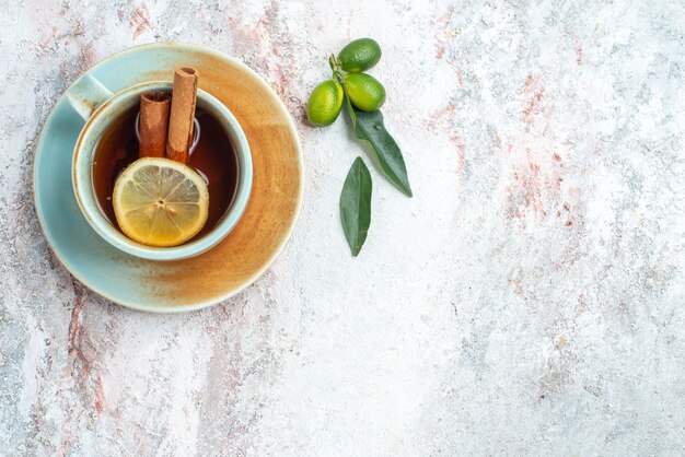 Vista superior de una taza de té blanco taza de té con rodajas de limón y palitos de canela en el platillo con frutas cítricas en la mesa rosa