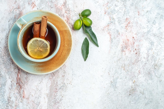 Vista superior de una taza de té blanco taza de té con rodajas de limón y palitos de canela en el platillo con frutas cítricas en la mesa rosa