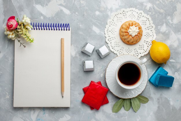 Vista superior de la taza de té caliente dentro de la taza blanca con el paquete de plata y el bloc de notas de caramelos de chocolate en el chocolate de la hora del té de galletas dulces ligeras