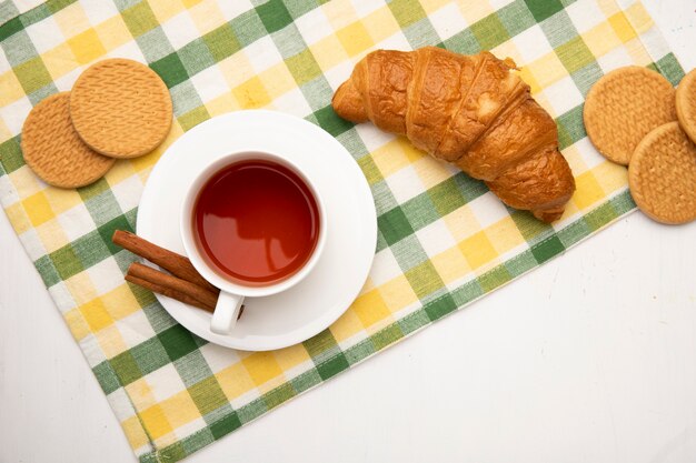 Vista superior de la taza de té con canela en bolsa de té y galletas con mantequilla japonesa roll sobre tela sobre fondo blanco con espacio de copia