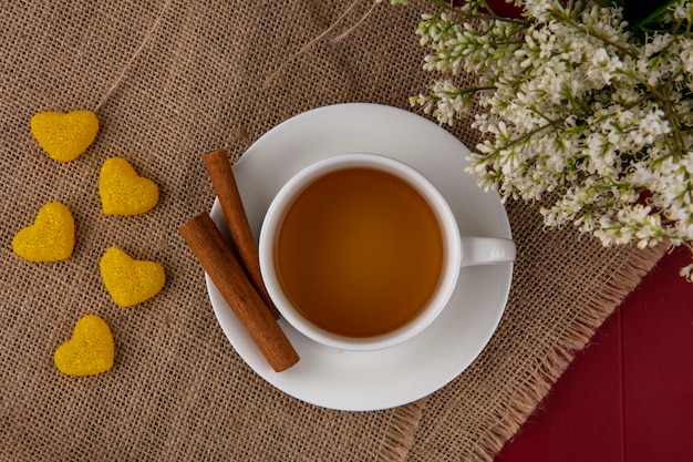 Vista superior de la taza de té con canela y flores en una servilleta beige