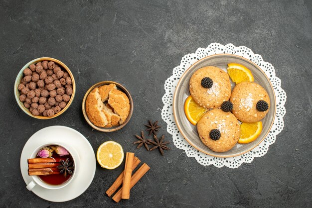 Vista superior de la taza de té con canela y galletas en la ceremonia de bebida de té de superficie gris oscuro dulce