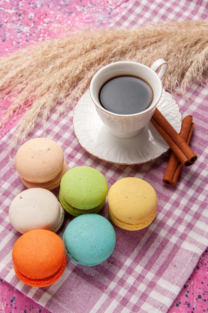 Vista superior de la taza de té con canela y macarons franceses en el escritorio de color rosa claro pastel galleta galleta azúcar dulce
