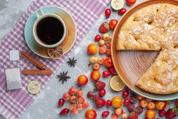 Vista superior de una taza de té con canela y pastel de frutas en el escritorio ligero, bebida de té, desayuno caliente