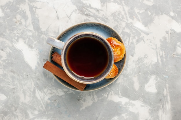 Vista superior de una taza de té con canela y pasteles pequeños en la superficie blanca