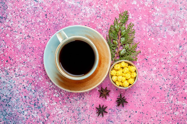Vista superior de la taza de té con caramelos amarillos en el escritorio rosa