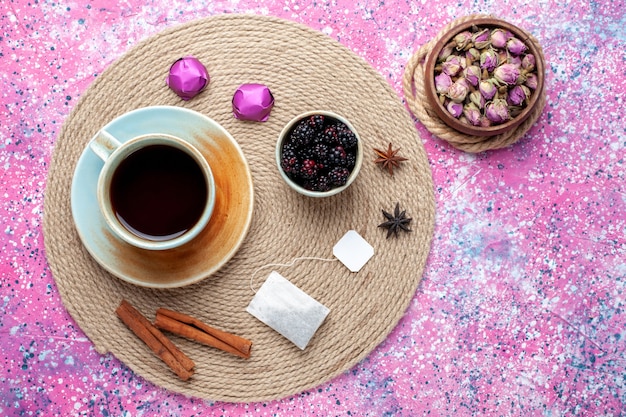 Vista superior de la taza de té con caramelos y canela sobre fondo rosa.