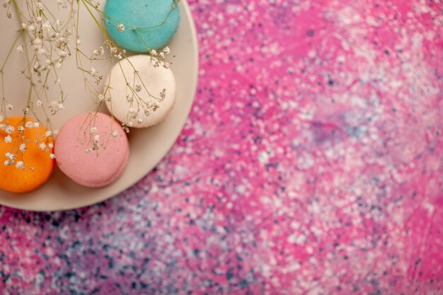 Vista superior de la taza de té con coloridos macarons franceses en el escritorio rosa