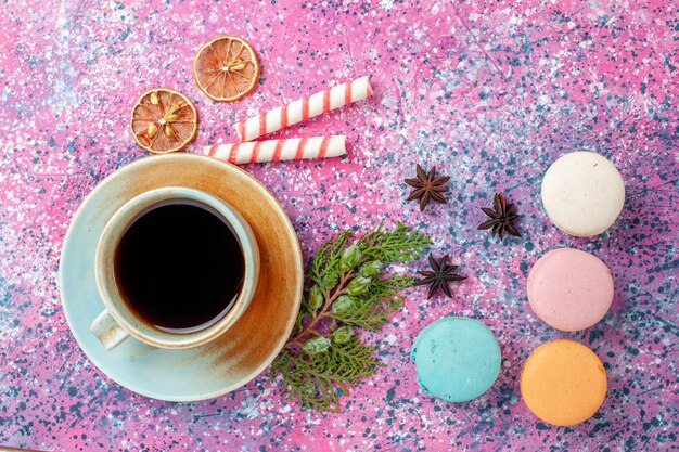 Vista superior de la taza de té con coloridos macarons franceses en el escritorio rosa