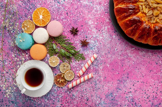 Vista superior de una taza de té con coloridos macarons franceses en la superficie rosa