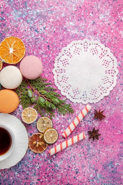 Vista superior de una taza de té con coloridos macarons franceses en la superficie rosa