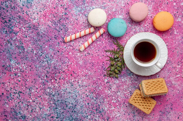 Vista superior taza de té con coloridos macarons franceses y waffles en la pared rosa pastel galleta azúcar dulce té de tarta