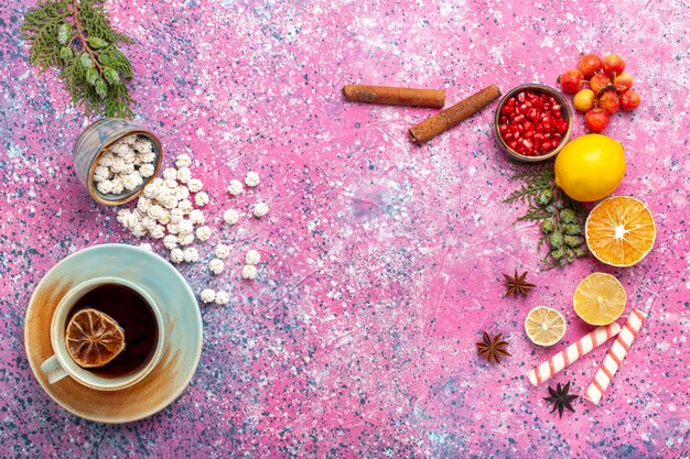 Vista superior de la taza de té con confituras dulces blancas y canela en el escritorio rosa claro