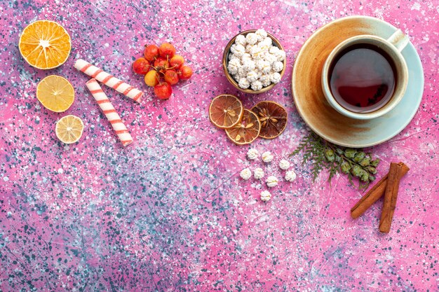 Vista superior de una taza de té con confituras dulces blancas en el escritorio rosa